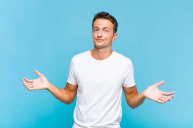 Genç yakışıklı adam şaşkın ve şaşkın, şüpheci, farklı seçenekleri tartıyor ya da komik bir ifadeyle seçiyor.