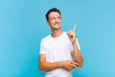 Genç yakışıklı adam mutlu bir şekilde gülümsüyor ve yan bakıyor, merak ediyor, düşünüyor ya da bir fikri var.