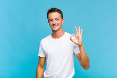 Genç yakışıklı adam mutlu, rahat ve tatmin olmuş hissediyor. Onayını iyi bir hareketle gösteriyor. Gülümsüyor.