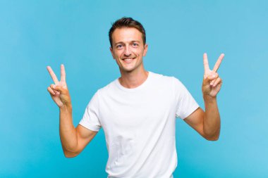 Genç yakışıklı adam gülümsüyor ve mutlu görünüyor, arkadaş canlısı ve memnun, işaret eden zafer ya da barış iki elle