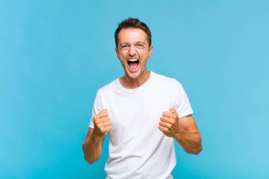 Genç yakışıklı adam sinirli, sinirli, sinirli bakışlar ve sıkı yumruklar ile agresif bir şekilde bağırıyor.