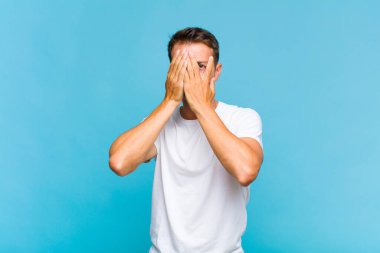 Genç yakışıklı adam elleriyle yüzünü kapatıyor, parmaklarının arasından şaşkın bir ifadeyle yan tarafa bakıyor.