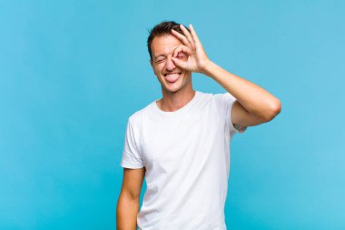 Genç yakışıklı adam mutlu bir şekilde gülümsüyor, şaka yapıyor ve gözetleme deliğinden bakıyor, sırları gözetliyor.