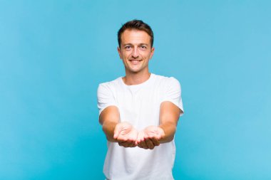 Genç yakışıklı adam mutlu bir şekilde gülümsüyor arkadaş canlısı, kendinden emin, olumlu bakışlı, bir nesne ya da konsept sunuyor ve gösteriyor.