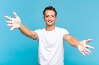 Genç yakışıklı adam neşeyle gülümsüyor sıcak, dostça, sevgi dolu bir kucak veriyor, mutlu ve sevimli hissediyor.