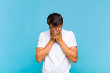 Genç yakışıklı adam üzgün, hayal kırıklığına uğramış, gergin ve depresif, iki eliyle yüzünü kaplayan, ağlayan