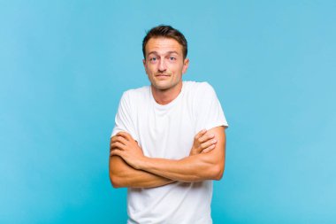 Genç yakışıklı adam omuz silkiyor, kafası karışık ve kararsız, kolları bağlı ve şaşkın görünüyor.