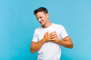 Genç yakışıklı adam üzgün, yaralı ve kalbi kırık görünüyor, iki elini de kalbine yakın tutuyor, ağlıyor ve bunalımda.