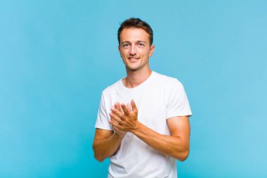 Genç yakışıklı adam kendini mutlu ve başarılı hissediyor, gülümsüyor ve alkışlıyor, alkışlarla tebrik ediyor.