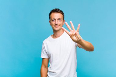 Genç yakışıklı adam gülümsüyor ve arkadaş canlısı görünüyor, 4 ya da 4 numarayı gösteriyor, eli önde, geri sayıyor.