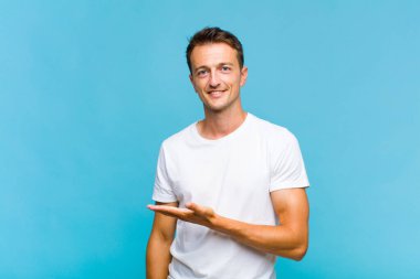 Genç yakışıklı adam neşeyle gülümsüyor, mutlu hissediyor ve fotokopi uzayında bir konsept gösteriyor.