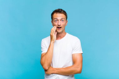 Genç yakışıklı adam şok ve inançsızlık içinde, elleri yanak ve kolları çapraz, sersemlemiş ve şaşırmış hissediyor.