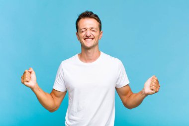 Genç yakışıklı adam çok mutlu ve şaşırmış görünüyor, başarıyı kutluyor, bağırıyor ve zıplıyor.