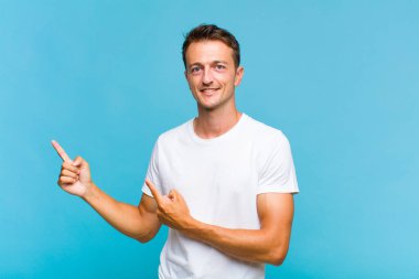 Genç yakışıklı adam mutlu bir şekilde gülümsüyor ve her iki elinde fotokopi alanında nesne gösteriyor.