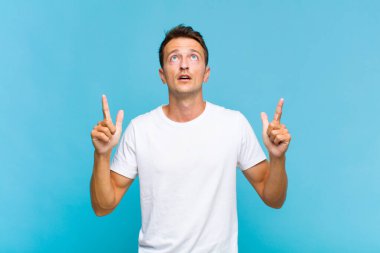 Genç yakışıklı adam şaşırmış, şaşırmış ve ağzı açık, iki eliyle uzayı göstererek