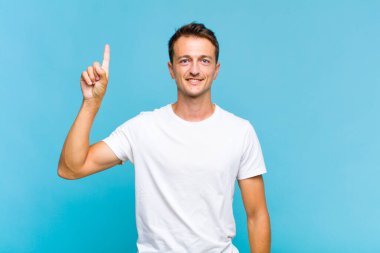 Genç yakışıklı adam neşeyle ve mutlulukla gülümsüyor, tek eliyle yukarıyı göstererek boşluğu kopyalıyor.