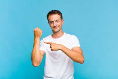 Genç yakışıklı adam sabırsız ve kızgın görünüyor, saati gösteriyor, dakiklik istiyor, zamanında gelmek istiyor.