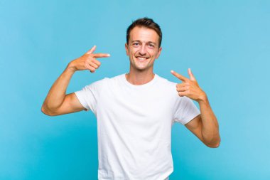 Genç yakışıklı adam, kendine güvenerek gülümsüyor. Geniş bir gülümseme, pozitif, rahat, tatmin olmuş bir tavır.