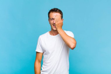 Genç yakışıklı adam uykulu, sıkılmış ve esniyor, baş ağrısı ve yüzünün yarısını kaplayan bir elle.