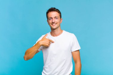 Genç yakışıklı adam mutlu, gururlu ve şaşırmış görünüyor, neşeli bir şekilde kendini gösteriyor, kendinden emin ve yüce hissediyor.
