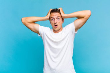 Genç yakışıklı adam heyecanlı ve şaşırmış görünüyor, ağzı açık, elleri başının üstünde, şanslı bir kazanan gibi hissediyor.