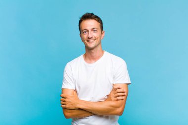 Genç yakışıklı adam mutlu, gururlu ve tatmin olmuş görünüyor. Kollarını kavuşturup gülümsüyor.