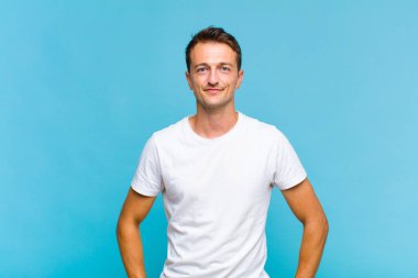 Genç yakışıklı adam pozitif ve kendinden emin gülümsüyor. Tatmin olmuş, arkadaş canlısı ve mutlu görünüyor.