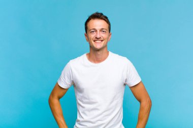 Genç yakışıklı adam mutlu ve şapşal görünüyor. Geniş, eğlenceli, kaçık bir gülüşü ve açık gözleri var.