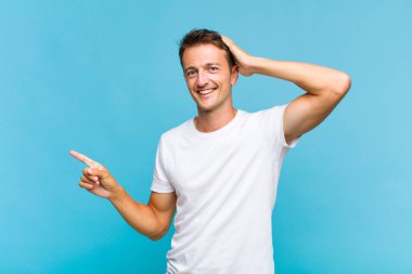 Genç yakışıklı adam gülüyor, mutlu, pozitif ve şaşırmış görünüyor. Yan fotokopi alanını işaret eden harika bir fikrin farkına varıyor.