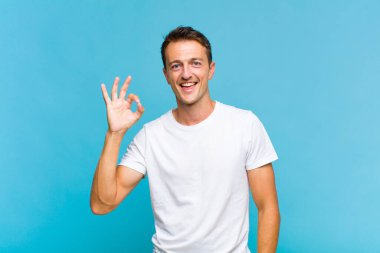 Genç yakışıklı adam kendini başarılı ve tatmin olmuş hissediyor, ağzı açık gülümsüyor, elle işaret veriyor.