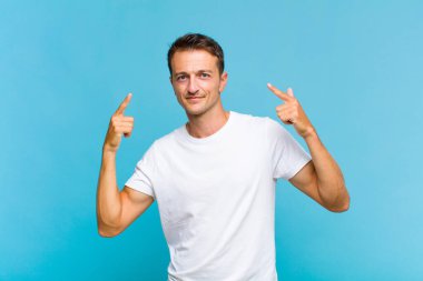 Kötü tavırlı genç yakışıklı adam gururlu ve agresif görünüyor, yukarıyı işaret ediyor ya da elleriyle alay işareti yapıyor.