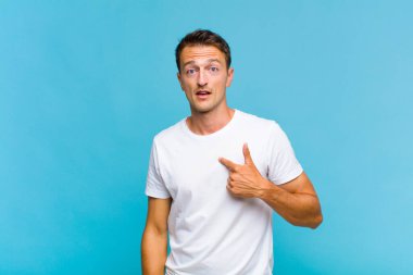 Şok olmuş ve ağzı açık, kendini işaret eden genç yakışıklı bir adam.