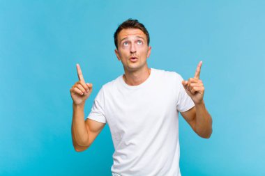 Genç ve yakışıklı bir adam şaşkınlık ve şaşkınlık dolu bakışlarla yukarıyı işaret ederek huşu içinde ve açık ağızlı hissediyor.