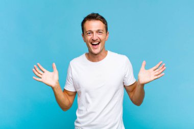 Genç yakışıklı adam mutlu ve heyecanlı görünüyor. Beklenmedik bir sürprizle şoke olmuş. İki eli yüzü açık.
