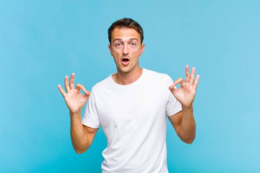 Genç yakışıklı adam şok olmuş, şaşırmış ve şaşırmış hissediyor. Onaylıyor. İki eliyle de onay işareti yapıyor.