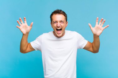 Genç ve yakışıklı bir adam panik ya da öfke içinde bağırıyor, şok olmuş, korkmuş ya da öfkeli, elleri başının yanında.