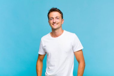 Genç ve yakışıklı bir adam neşeli, neşeli, mutlu, kendinden emin ve rahat bir ifadeyle gülümsüyor.