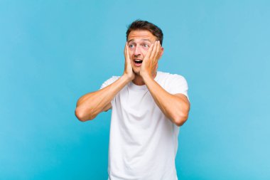 Genç yakışıklı adam mutlu, heyecanlı ve şaşırmış hissediyor, iki eli yüzü yana bakıyor.