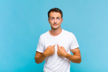Genç ve yakışıklı bir adam kendini işaret ediyor. Şaşırmış ve şaşırmış bir şekilde bakıyor.