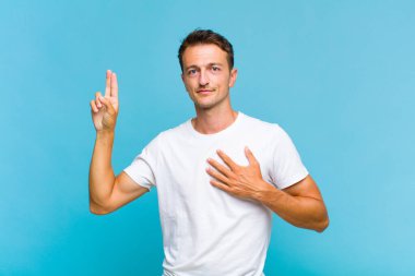 Genç yakışıklı adam mutlu, kendinden emin ve güvenilir görünüyor, gülümsüyor ve zafer işareti gösteriyor, olumlu bir tavırla.