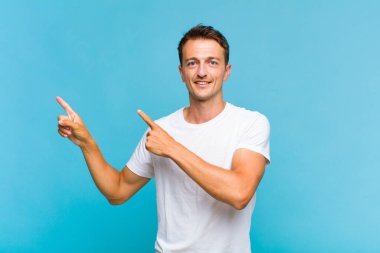 Genç, yakışıklı bir adam kendini neşeli ve şaşırmış hissediyor. Şok olmuş bir ifadeyle gülümsüyor ve bir tarafı işaret ediyor.