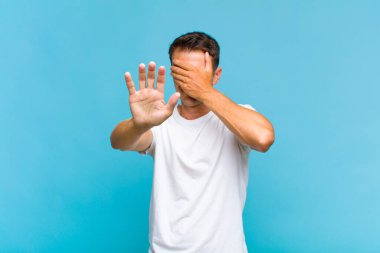 Genç ve yakışıklı bir adam elleriyle yüzünü kapatıyor ve kamerayı durdurmak için diğer elini öne koyuyor. Fotoğraf ya da resimleri reddediyor.