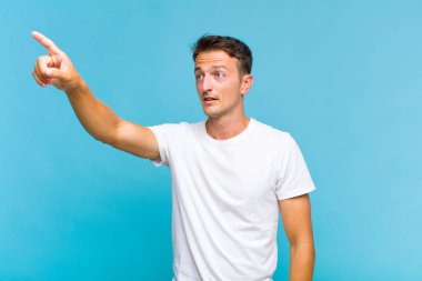 Genç yakışıklı adam şaşkın ve şaşırmış hissediyor, hayranlıkla yukarı bakıyor, şaşırmış, ağzı açık bakıyor.