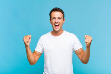 Genç yakışıklı bir adam sinirli bir ifadeyle ya da yumruklarıyla başarıyı kutlarken agresif bir şekilde bağırıyor.