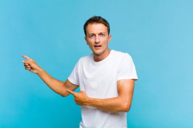 Genç yakışıklı adam şaşkın ve şaşırmış hissediyor. Kenardaki fotokopi alanını işaret ediyor. Şaşırmış, ağzı açık bir bakış.