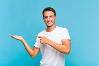 Genç yakışıklı adam neşeyle gülümsüyor ve bir objeyi göstererek veya reklamını yaparak avucundaki fotokopi alanını gösteriyor.