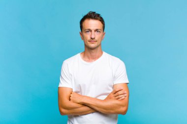 Genç yakışıklı adam hayal kırıklığına uğramış ve hayal kırıklığına uğramış, ciddi görünüyor, kızgın ve kollarını kavuşturmuş.