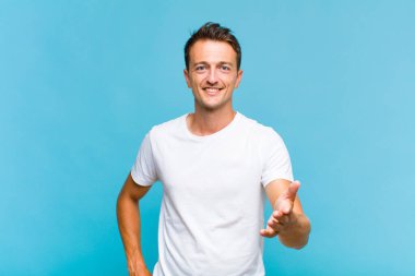 Genç yakışıklı adam gülümsüyor, mutlu görünüyor, kendinden emin ve arkadaş canlısı, bir anlaşmaya varmak için el sıkışıyor, işbirliği yapıyor.