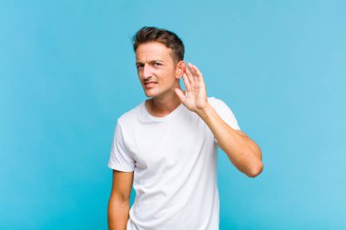 Genç yakışıklı adam ciddi ve meraklı görünüyor, dinliyor, gizli bir konuşma veya dedikodu duymaya çalışıyor, kulak misafiri oluyor.