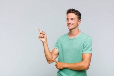 Genç yakışıklı adam mutlu bir şekilde gülümsüyor ve yan bakıyor, merak ediyor, düşünüyor ya da bir fikri var.